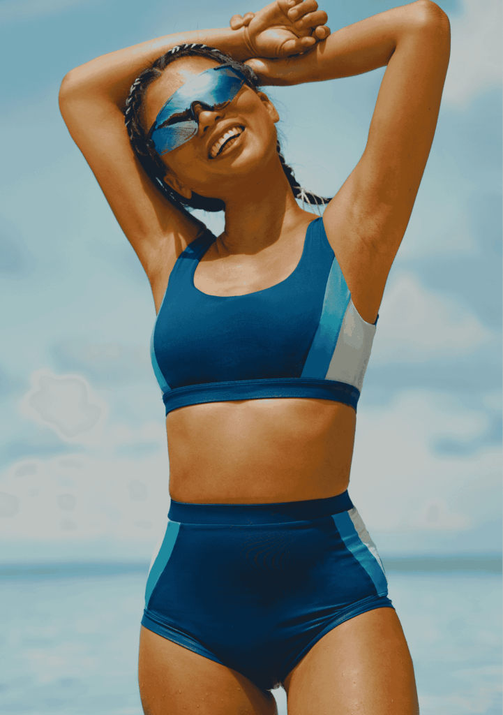 A happy woman running joyfully on the sandy beach in a white Leda Sport one-piece, made from breathable fabric perfect for land-based coastal activities.