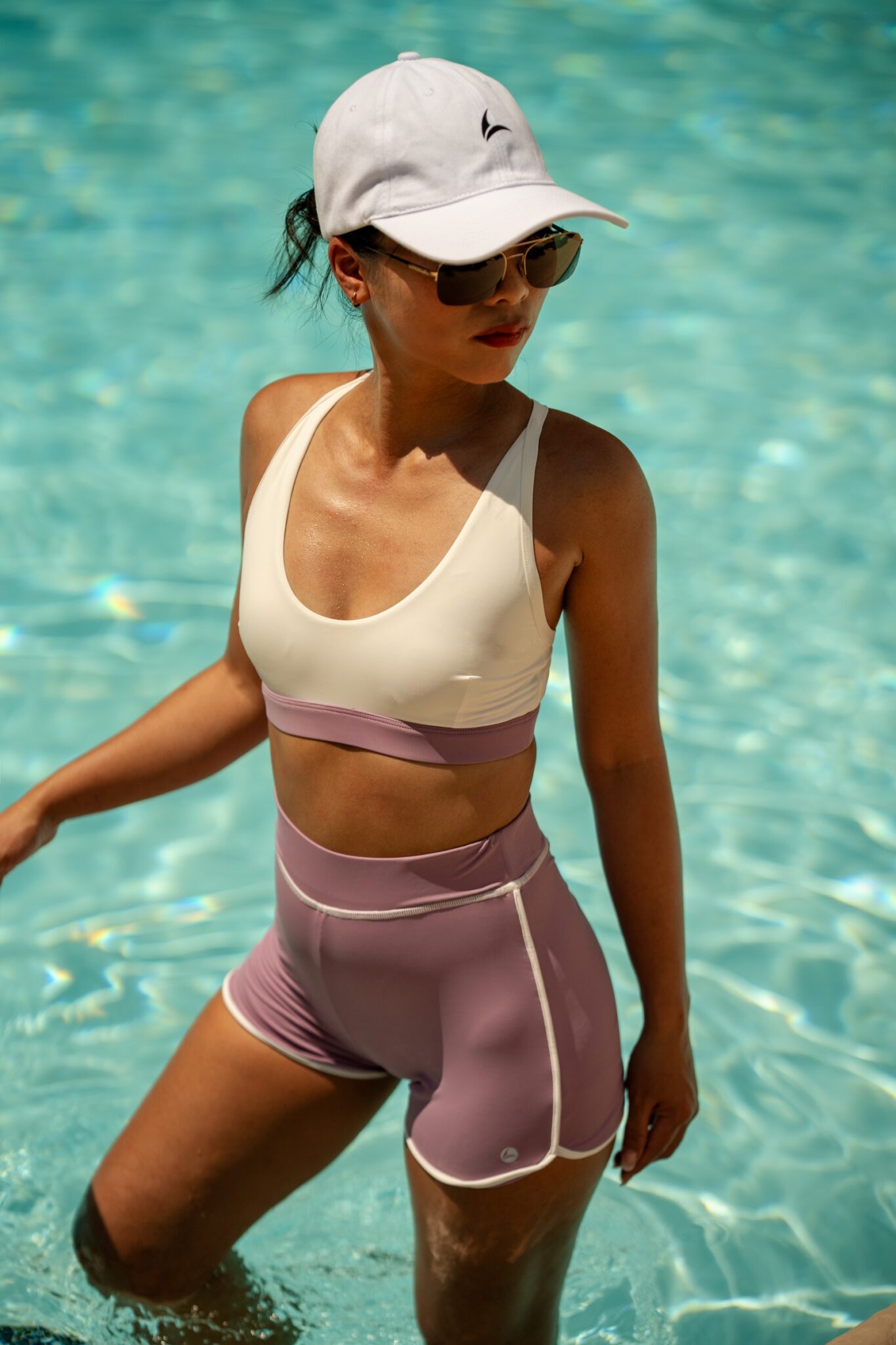 Woman wearing a cream and pink Leda Sport swim set in a sunlit pool