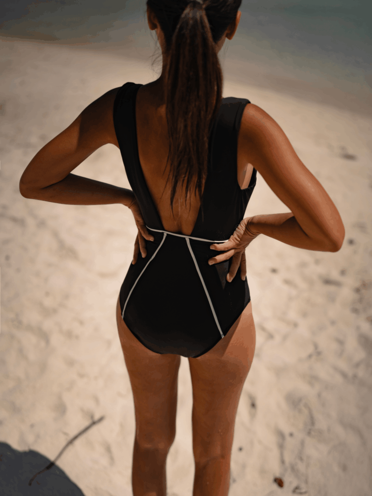 Back view of the trapezoid open back and white piping on the black Alma one-piece