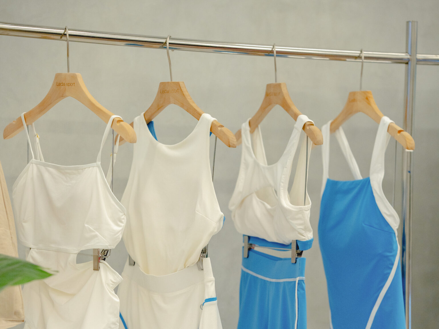 Leda Sport swimsuits in white and blue hanging on wooden Leda Sport hangers