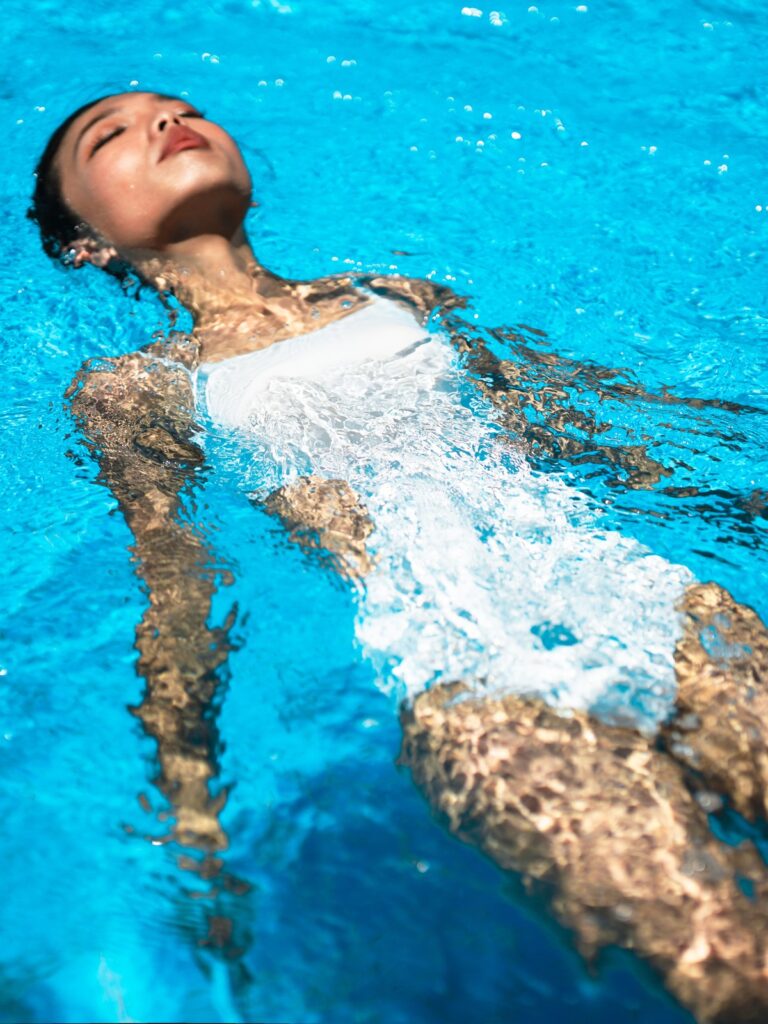Woman floating on her back in a pool in the cream white Viva one-piece