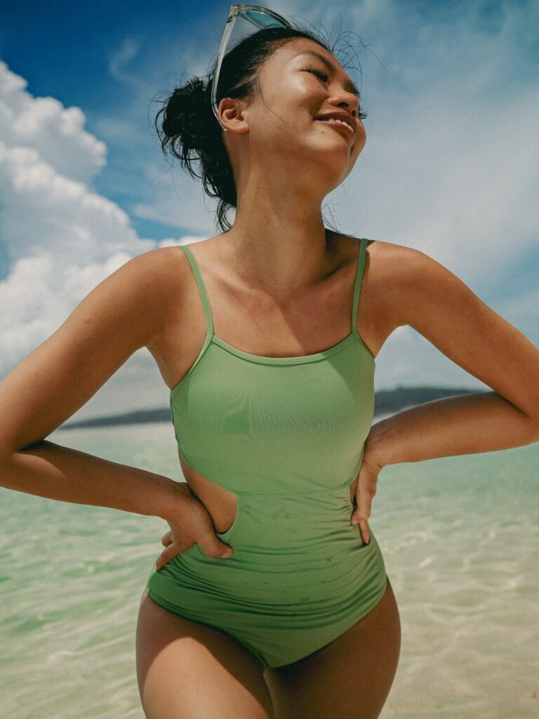 Smiling woman on the beach in the matcha green Viva one-piece