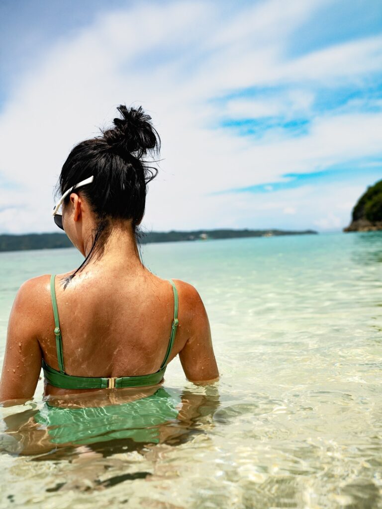 Woman wading into clear water in the matcha green Viva one-piece