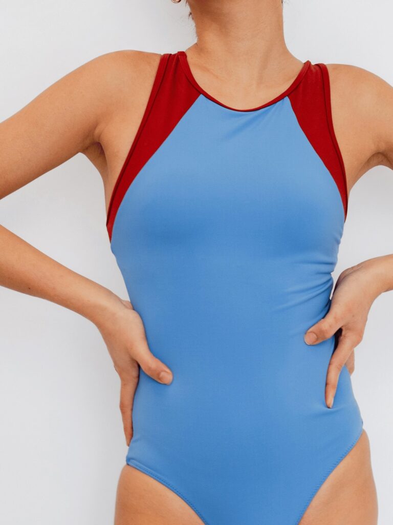 Close-up of the high round neck and syrah red shoulder panels on the cornflower blue Mira one-piece