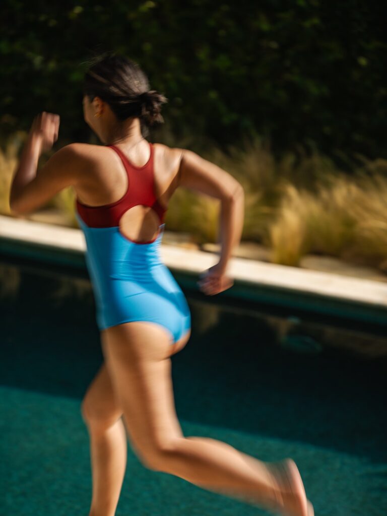 Woman running along a pool edge in the cornflower blue Mira one-piece