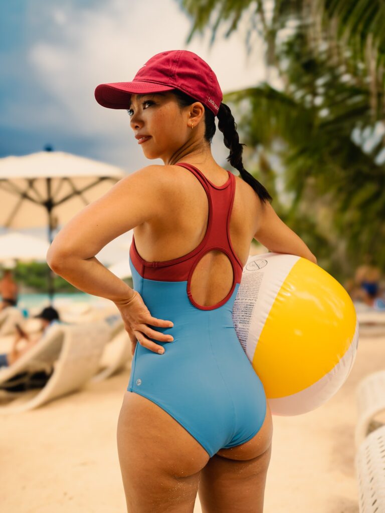 Woman with a beach ball in the cornflower blue Mira one-piece