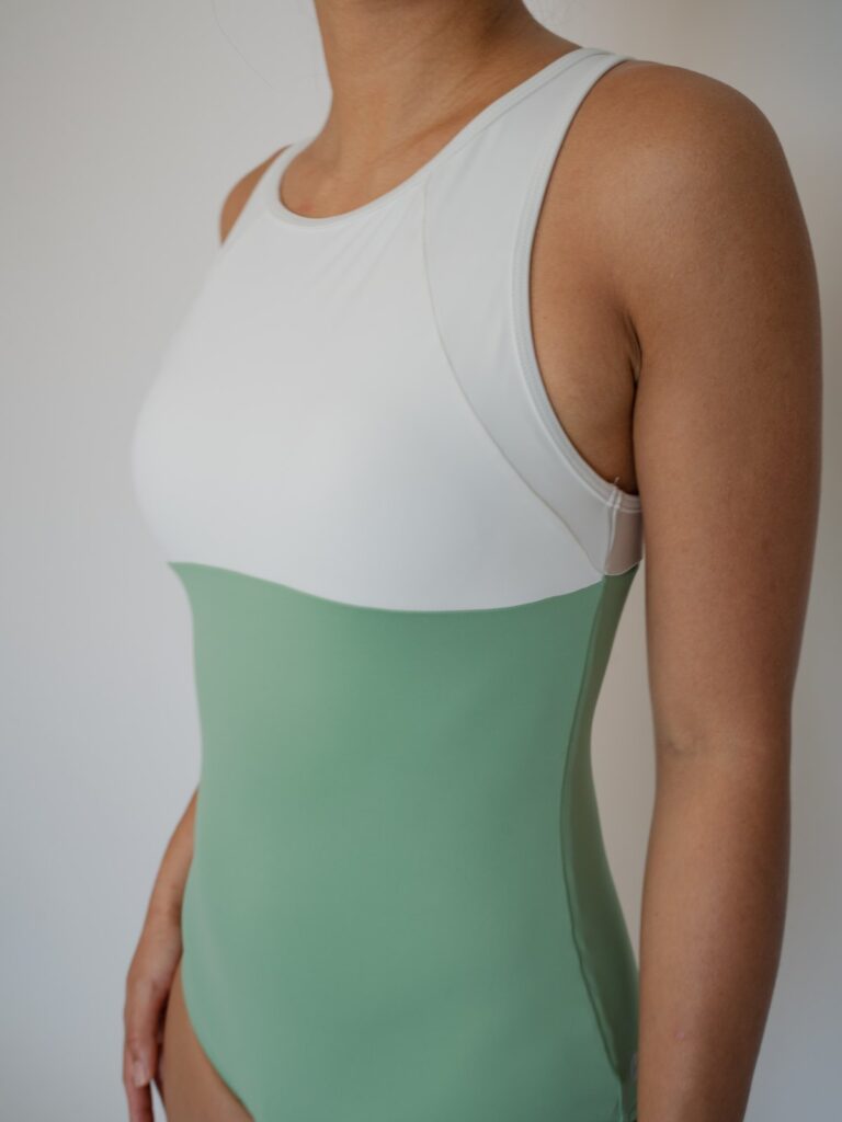 Close-up of the high round neck and wide straps on the white and matcha green Mira one-piece