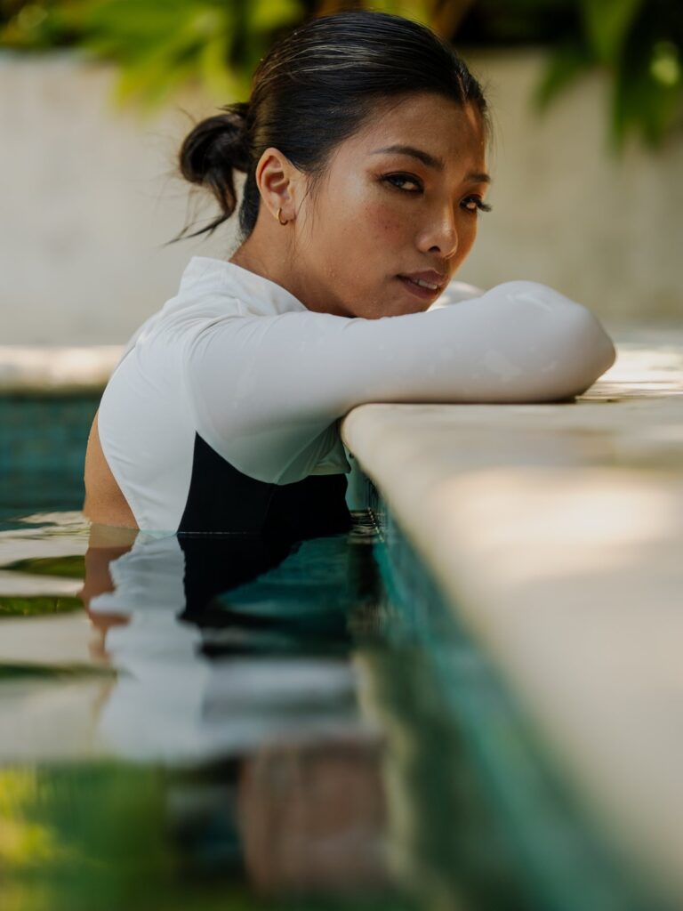 Woman resting on the pool edge in the Rosa long-sleeve one-piece