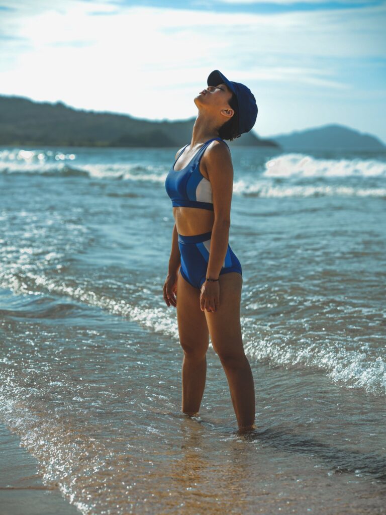 Woman standing at the water's edge on a beach in the royal blue Zeta two-piece