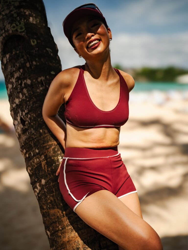 Woman laughing against a palm tree on the beach in the Cala top and boyshort