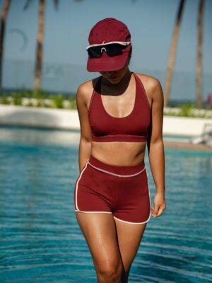Woman outdoors at a resort wearing the Cala two-piece in syrah red: U-neck cross-back swim top and high-waist boyshort