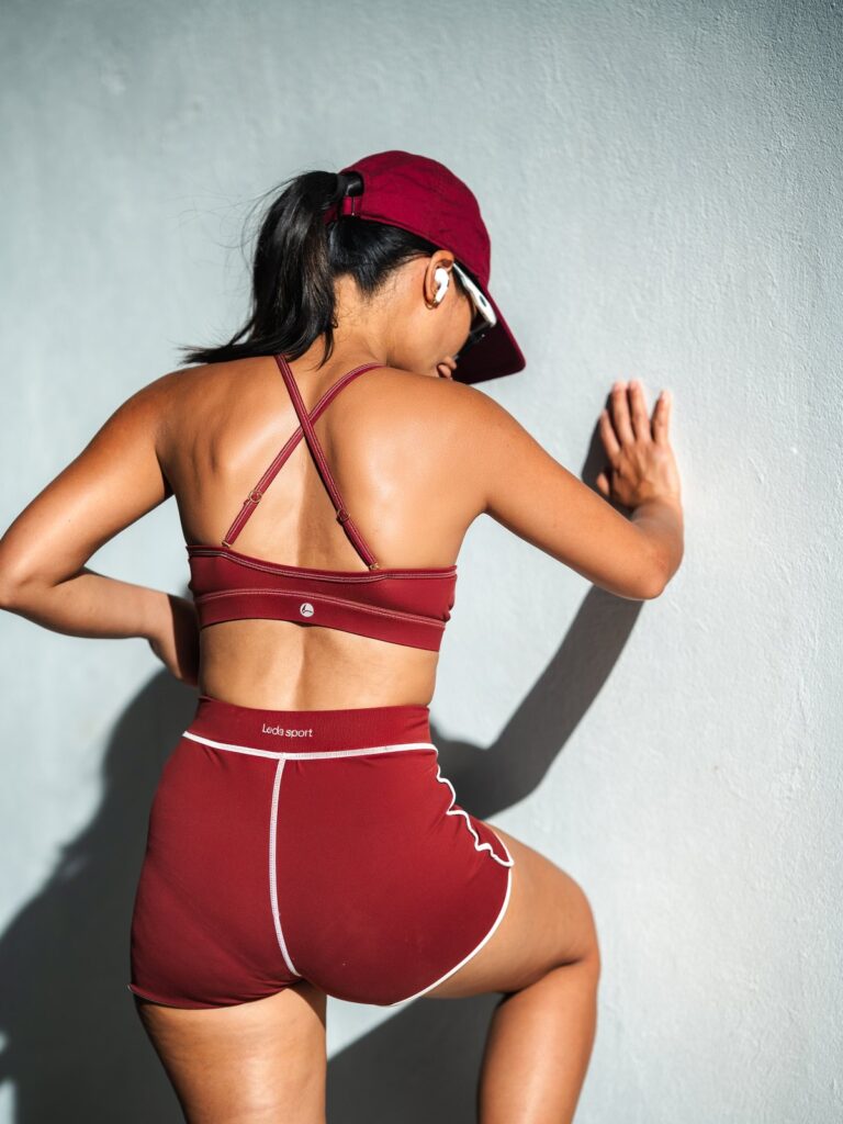 Woman leaning on a white wall in the syrah red Cala top and high-waist boyshort, seen from the back