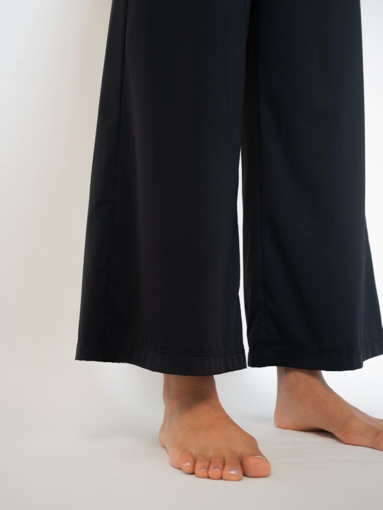 Close-up of the wide cropped hem of the black pull-on pants above bare feet