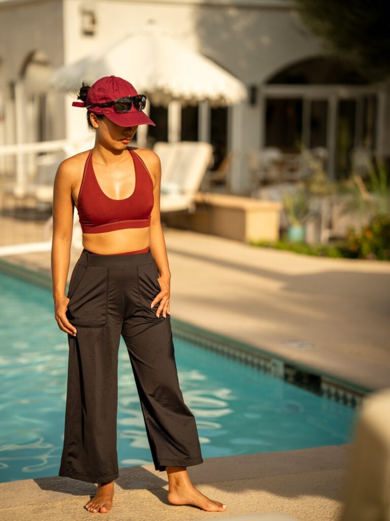 Woman standing by a resort pool in the black wide-leg cropped pants and a red sports top