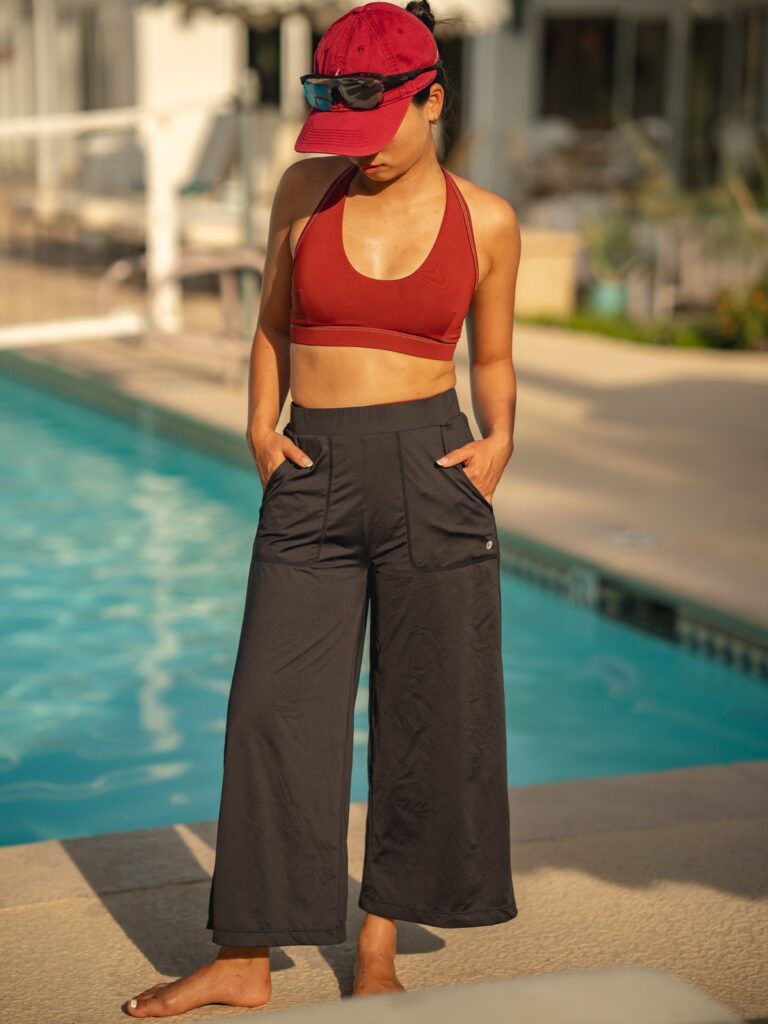 Woman with hands in the pockets of the black wide-leg cropped pull-on pants by a pool
