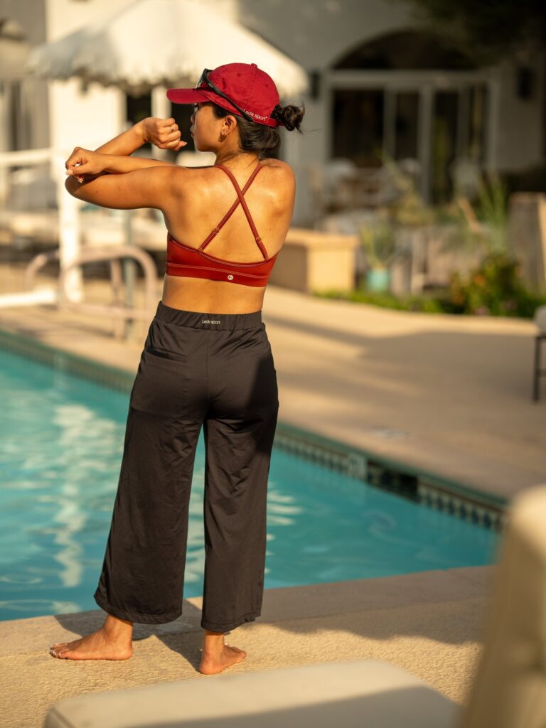 Woman stretching by a pool in the black wide-leg cropped pants and a red swim top