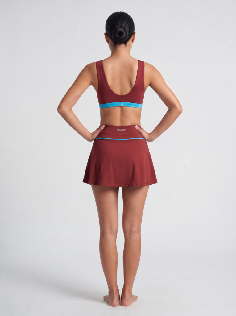 Model in the syrah red Siena cutout swim top and high-waist swim skort, full-length back view on a white background