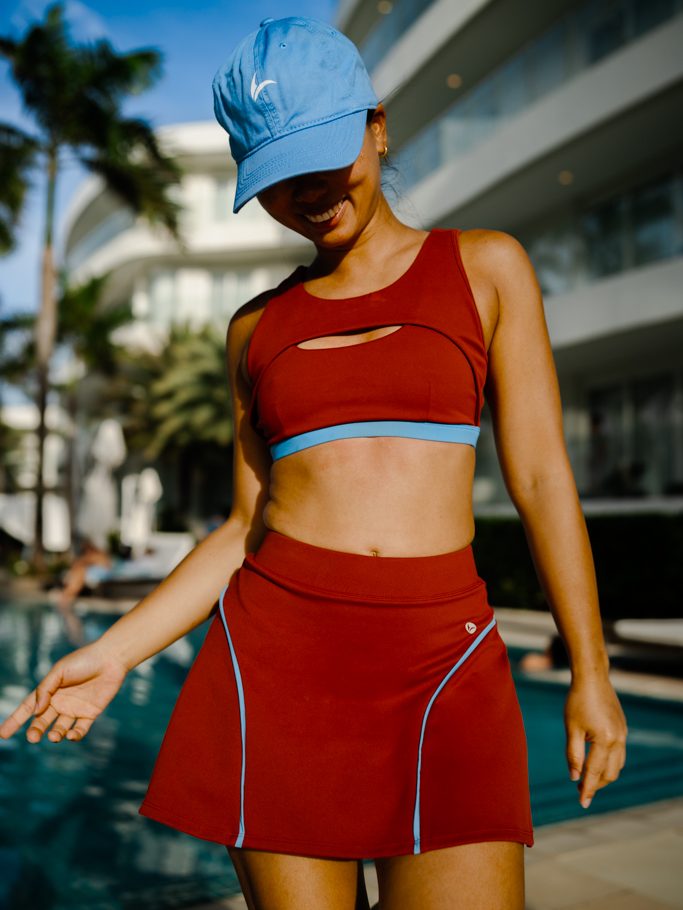 Woman in a light blue cap by a pool wearing the syrah red Siena cutout swim top